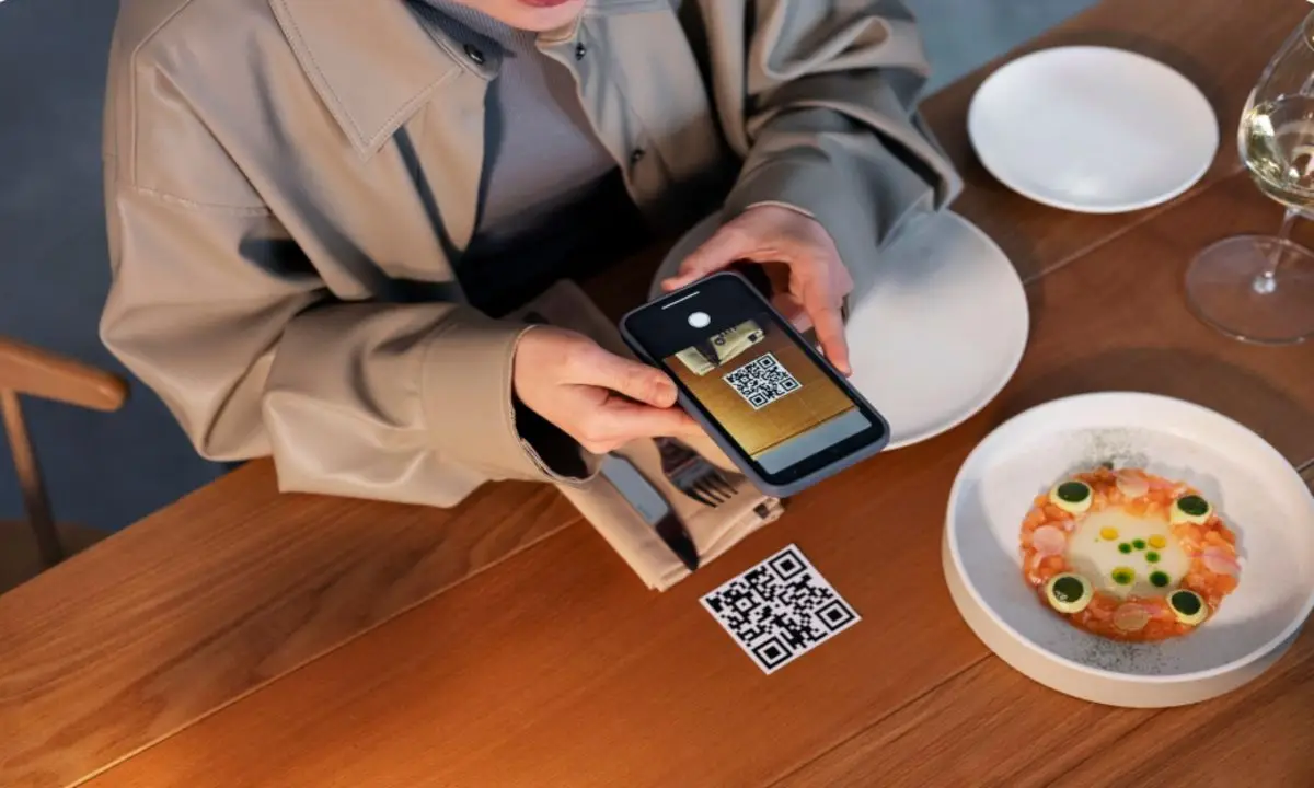 What Are the Advantages of QR Code Ordering for Hotels? 2 Guest scanning a QR code on a restaurant table using smartphone for contactless hotel food ordering and digital menu access.