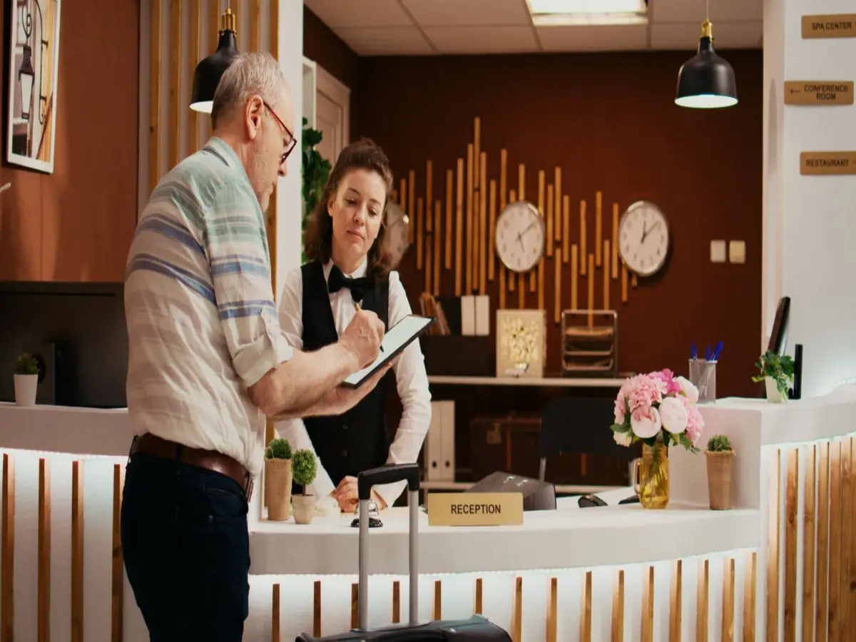 How Can Hotels Reduce Front Desk Wait Times During Peak Check-In Hours? 3 Hotel receptionist assisting a guest with check-in documents at the reception desk